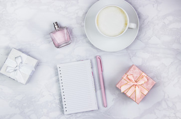 Women's accessories on a white marble table. Notepad, pen and glass of coffee on the table and other female cosmetic accessories. Beauty and fashion concept. Top view, flat lay, copy space