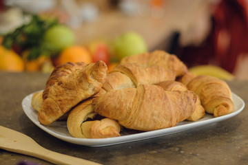Freshly baked croissants on a white plate on a wooden table. Delicious breakfast on the background of fresh vegetables, fruits