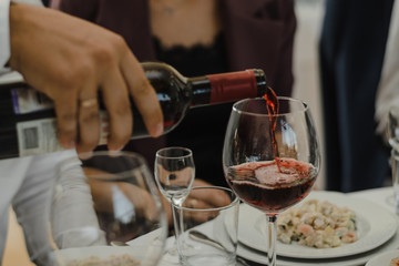 The man, the waiter pours red wine by the glass.