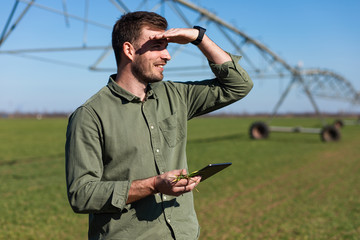 Young farmer standing in wheat field and setup irrigation system on tablet.