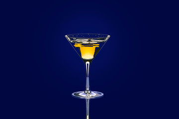Yellow-red cocktail in baikal for martini with a beautiful splash against drops on a blue background.