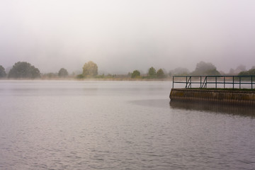 view of misty water surface with pier and trees