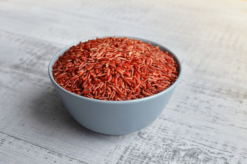 Fototapeta na wymiar Bowl with uncooked red rice on wooden background