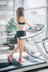 Attractive muscular smiling fitness woman running on treadmill in gym