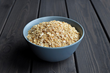 Rolled oats in ceramic bowl on dark wooden background