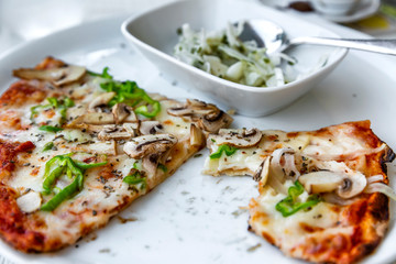 Unfinished pieces of pizza on a plate in an open-air restaurant. Close-up.