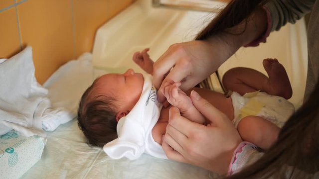 Young mother puts clothes on infant baby child - pants, sweater and bodykit before discharge from maternity hospital