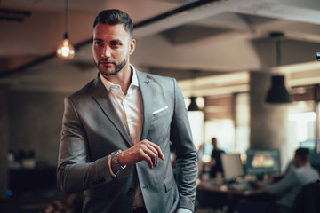 Portrait of young businessman in suit looking at his watch - obrazy, fototapety, plakaty