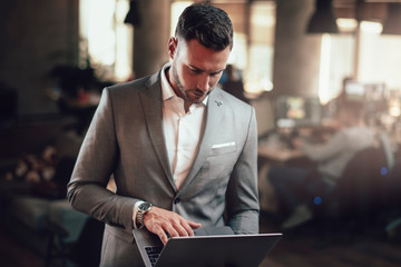 Attractive businessman standing in the office with his laptop