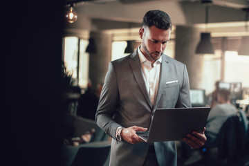 Attractive businessman standing in the office with his laptop