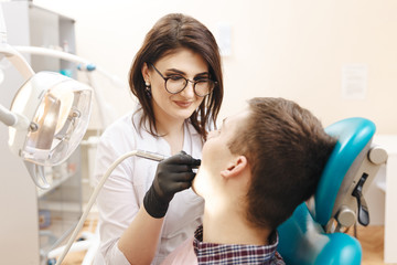 Picture of young female dentist in white coat working with male patient in the dental room