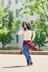 Street hip hop dancer on sunny day. Young happy sportive woman in urban background listening music in white wireless headphones and dancing. Hair fluttering in the wind