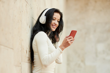 Young woman listening to music via wireless headphones on the street. holding mobile phone in hands 