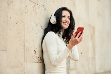 Young woman listening to music via wireless headphones on the street. holding mobile phone in hands 