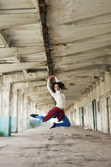 Street dancer. Young woman jumping high on industrial background on sunny day. 