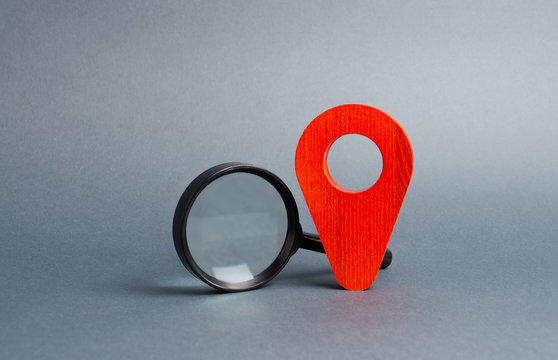 Red location pointer and a Magnifying glass on a gray background. Tourism and travel. Spying on the citizens.. Orientation around the city, location of events Concept of navigation and venue.