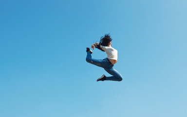 Modern young street dancer jumping high on a blue sky background. Woman flies up to the sun