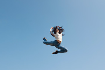 Modern young street dancer jumping high on a blue sky background. Woman flies up to the sun