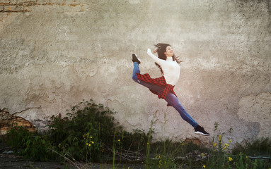 Modern young street dancer jumping high on the urban wall background. Woman flies up to the sun