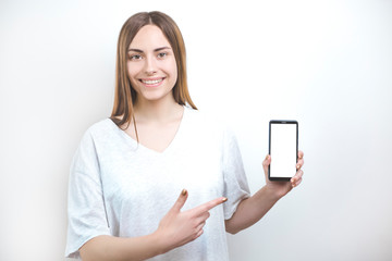 Smiling female shows finger on smartphone with white screen. 