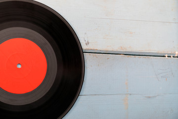 Black long-play vinyl record with red label on light blue rustic wooden background.