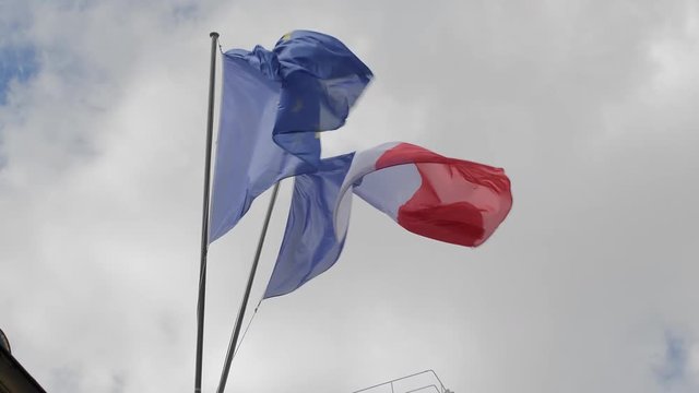 The flag of France and the European Union waves in the wind. Against the backdrop of a cloudy sky. Slow Motion.