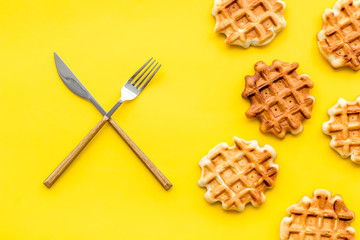 Breakfast with Belgian waffles with knife and fork on yellow background top view