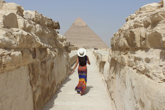 woman walking in between beige rocks towards pyramid