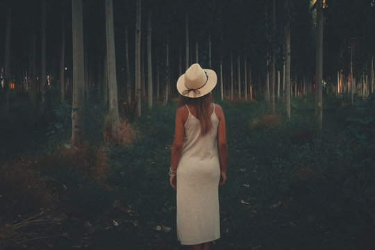 woman wearing white spaghetti strap dress with hat between trees during daytime