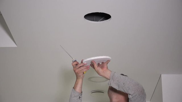 Electrician with handsaw saw hole in gypsum ceiling for lighting installation