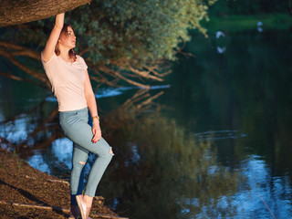 Beautiful girl walking along the river at sunset. Enjoy the warm summer evenings