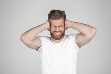 Portrait of beautiful sexy bearded man. holds his arms behind his head and shouts. he has a headache, he stands in front of the white background