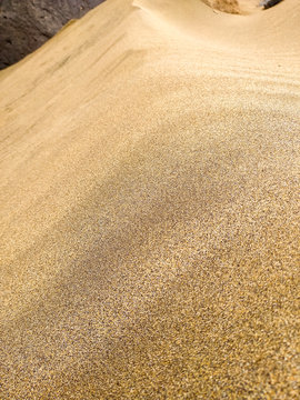 close up of a sand golden dune in the desert with million of grains of sand in a sunny day with a black stone at the back of the picture. Vertical photo