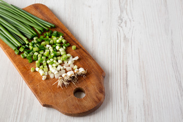 Chopped green onions on a rustic wooden board over white wooden background, side view. Space for text.