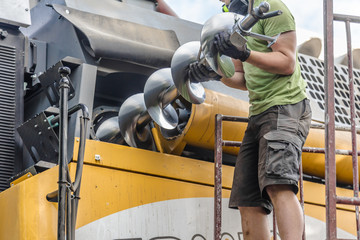 The mechanics repair the yellow and green combine harvester in the farm yard. 