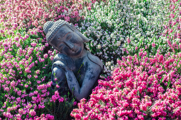 Peaceful garden. Traditional serene buddha statue ornament with beautiful flowers.