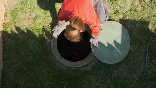 Girl plumber looks into an open draining manhole. top view. Service of the house individual sewerage.