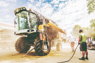 The mechanics repair the yellow and green combine harvester in the farm yard. 