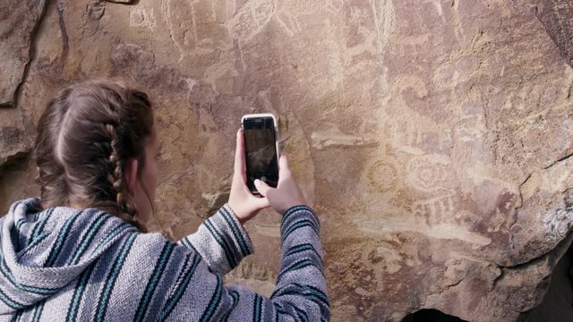 Woman raising phone to take picture of petroglyphs found throughout Nine Mile Canyon in Utah.