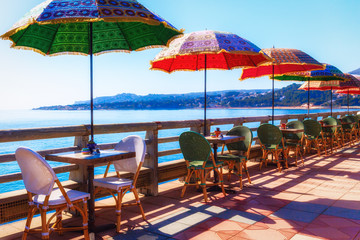Multi-colored umbrellas against the background of the sea in coastal cafe limited by a wooden handrail.