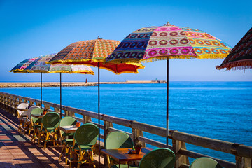 Multi-colored umbrellas against the background of the sea in coastal cafe limited by a wooden handrail.
