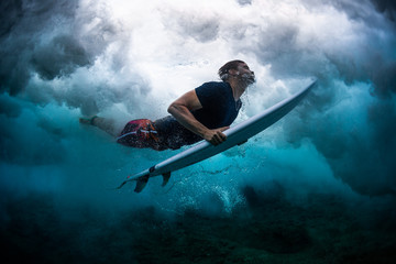 Young male surfer dives under the broken wave with his surfboard - obrazy, fototapety, plakaty
