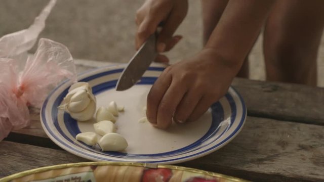 Handheld, medium close up of a person cutting up garlic with a large knife.
