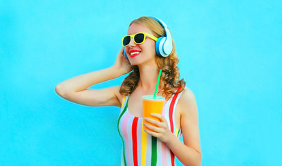 Portrait happy smiling woman holding cup of juice listening to music in wireless headphones on colorful blue background
