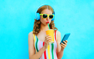 Portrait cool girl drinking fruit juice holding phone listening to music in wireless headphones on...