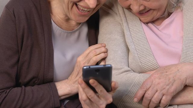 Happy women watching funny photos on smartphone and laughing, remembering past