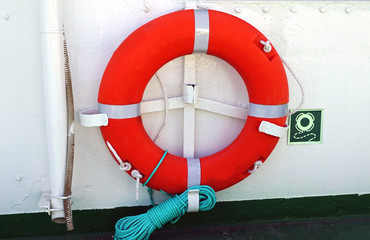 Red lifebuoy aboard ship, white wall.