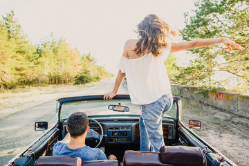 young beautiful couple driving a cabriolet car at sunset