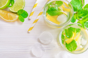Refreshing summer drink mojito with lime, lemon and mint, with ice cubes on white wooden background. Flat-lay, top view.