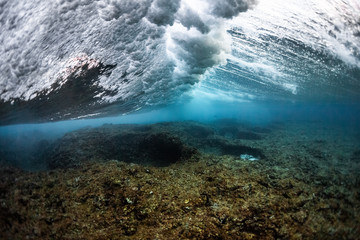 Underwater view of the ocean wave breaking over the shallow part of the coral reef at Honkeys surf spot in the Maldives
